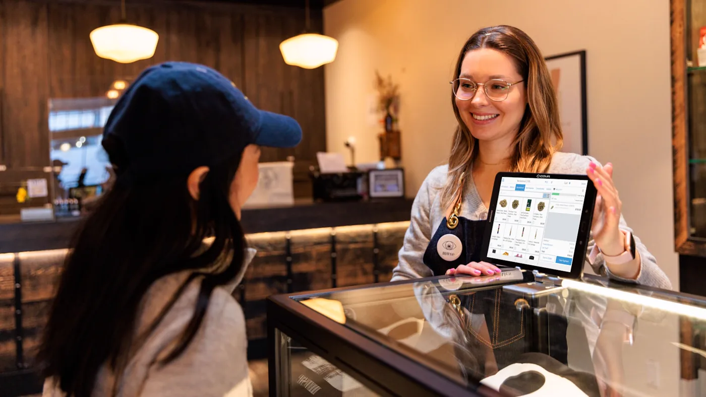 A shop employee showing a customer an online storefront on a tablet across the counter.